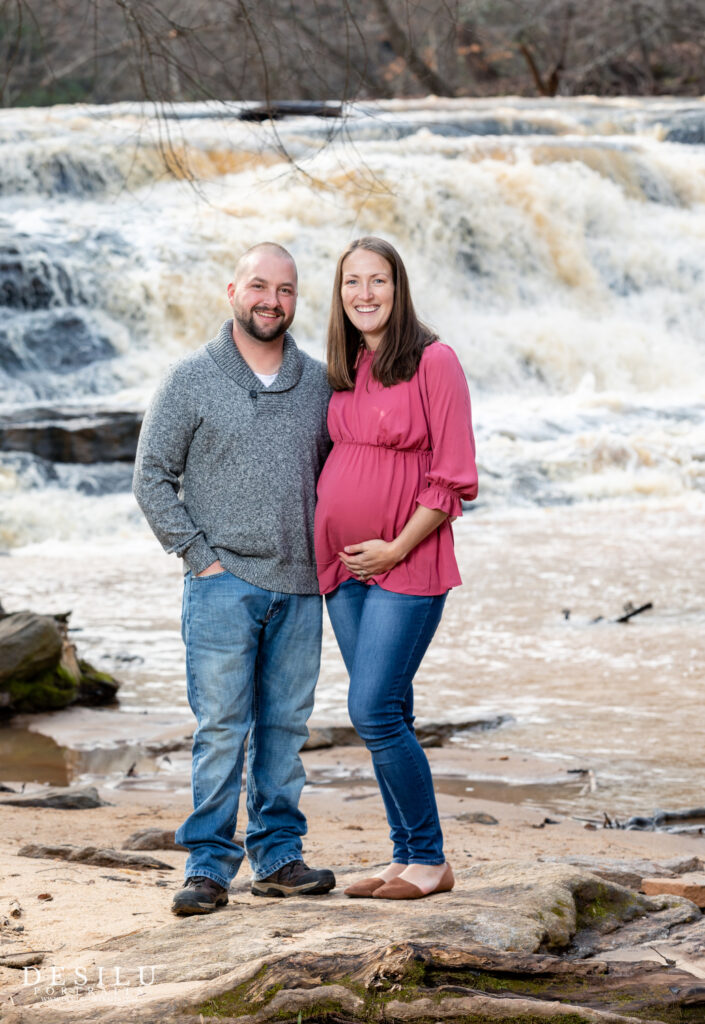 A man and pregnant woman standing in front of a waterfall