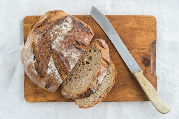 Sourdough loaf partially sliced on a wooden cutting board with knife resting next to it