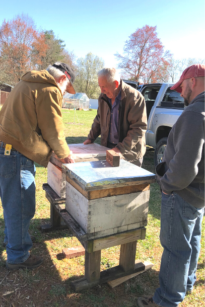 3 men installing 2 bee hives on a stand