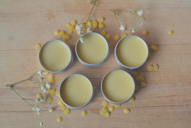 5 homemade lip balm tins surrounded by beeswax pellets and white flowers