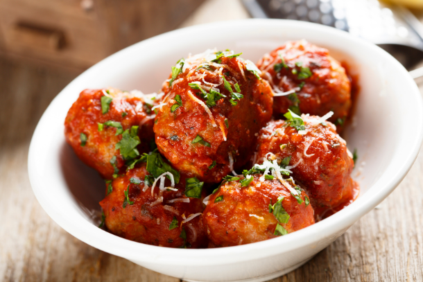 Grain-free meatballs covered in sauce, cheese, and herbs in a white bowl