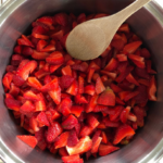 Chopped strawberries in a stock pot with a wooden spoon being prepped for easy and healthy strawberry chis seed jam