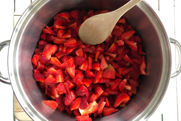 Chopped strawberries in a stock pot with a wooden spoon being prepped for easy and healthy strawberry chis seed jam